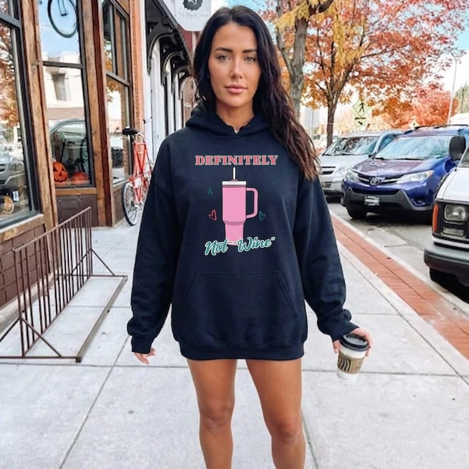 Woman wearing a black hoodie with text and graphics, standing on a sidewalk.