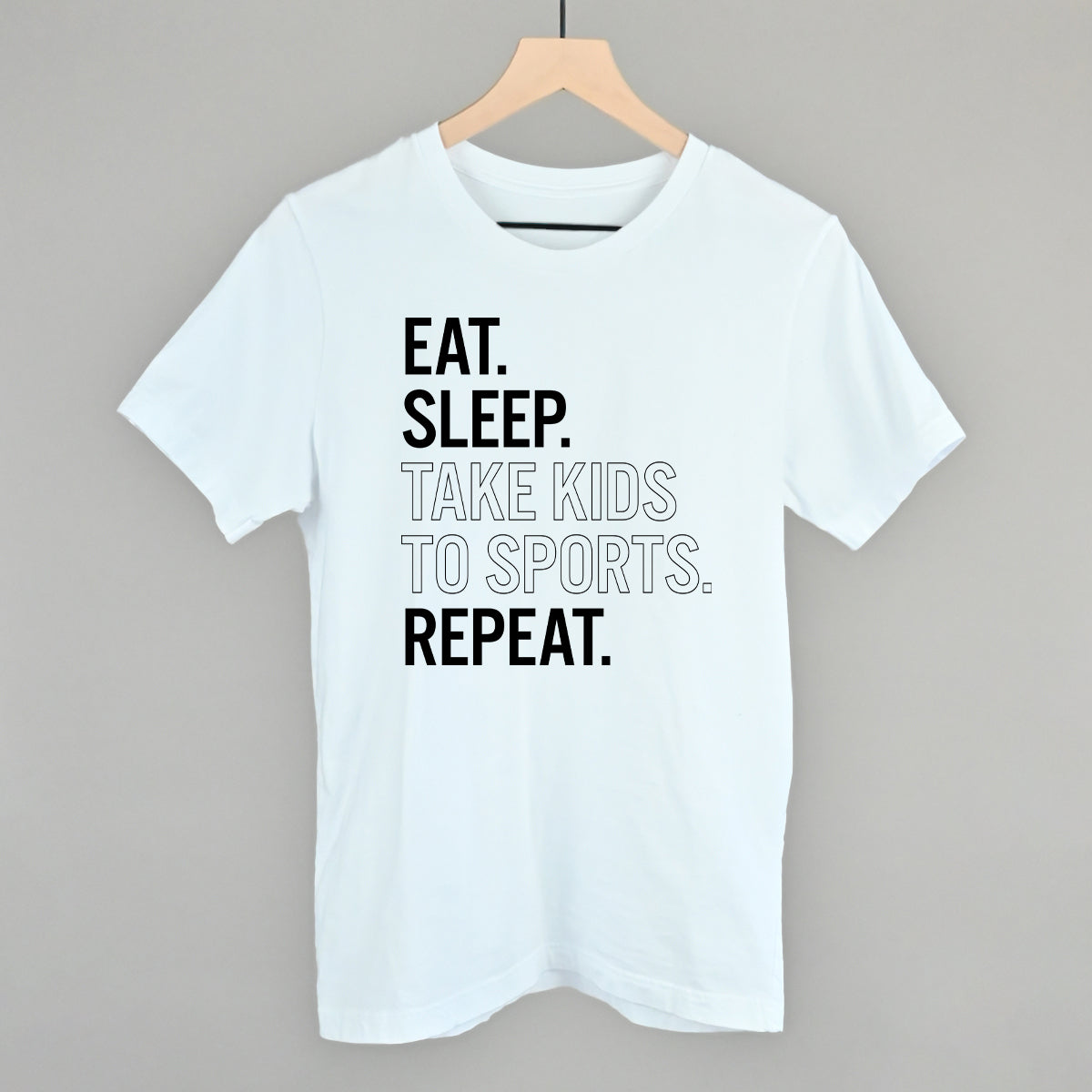 Collection of White t-shirt with text 'EAT. SLEEP. TAKE KIDS TO SPORTS. REPEAT.' on a hanger against a gray background in a gallery layout