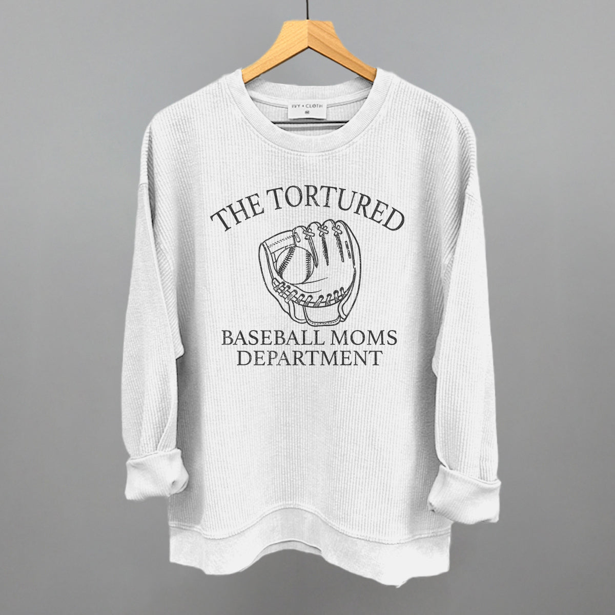 White sweatshirt with graphic and with 'The Tortured Baseball Moms Department' text on a hanger against a gray background