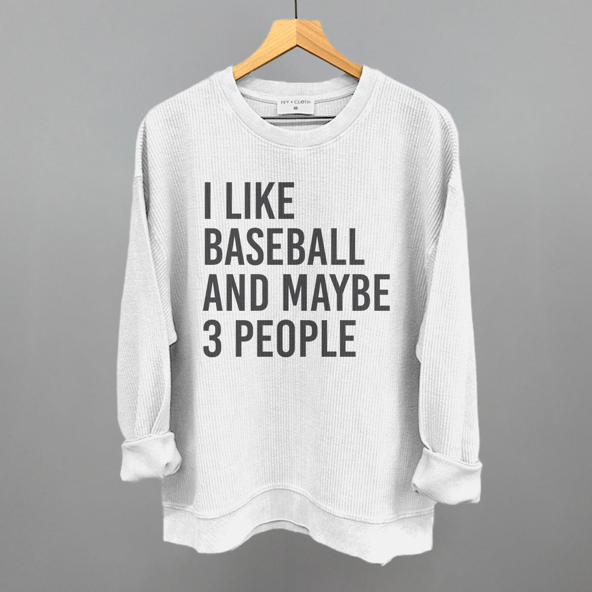 White sweatshirt with text 'I LIKE BASEBALL AND MAYBE 3 PEOPLE' on a hanger against a gray background