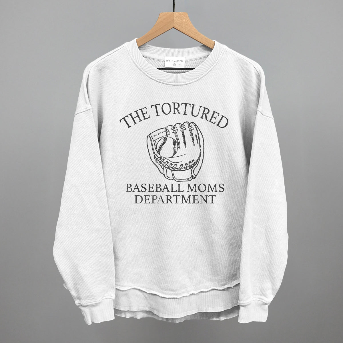 White sweatshirt with graphic and with 'The Tortured Baseball Moms Department' text on a hanger against a gray background
