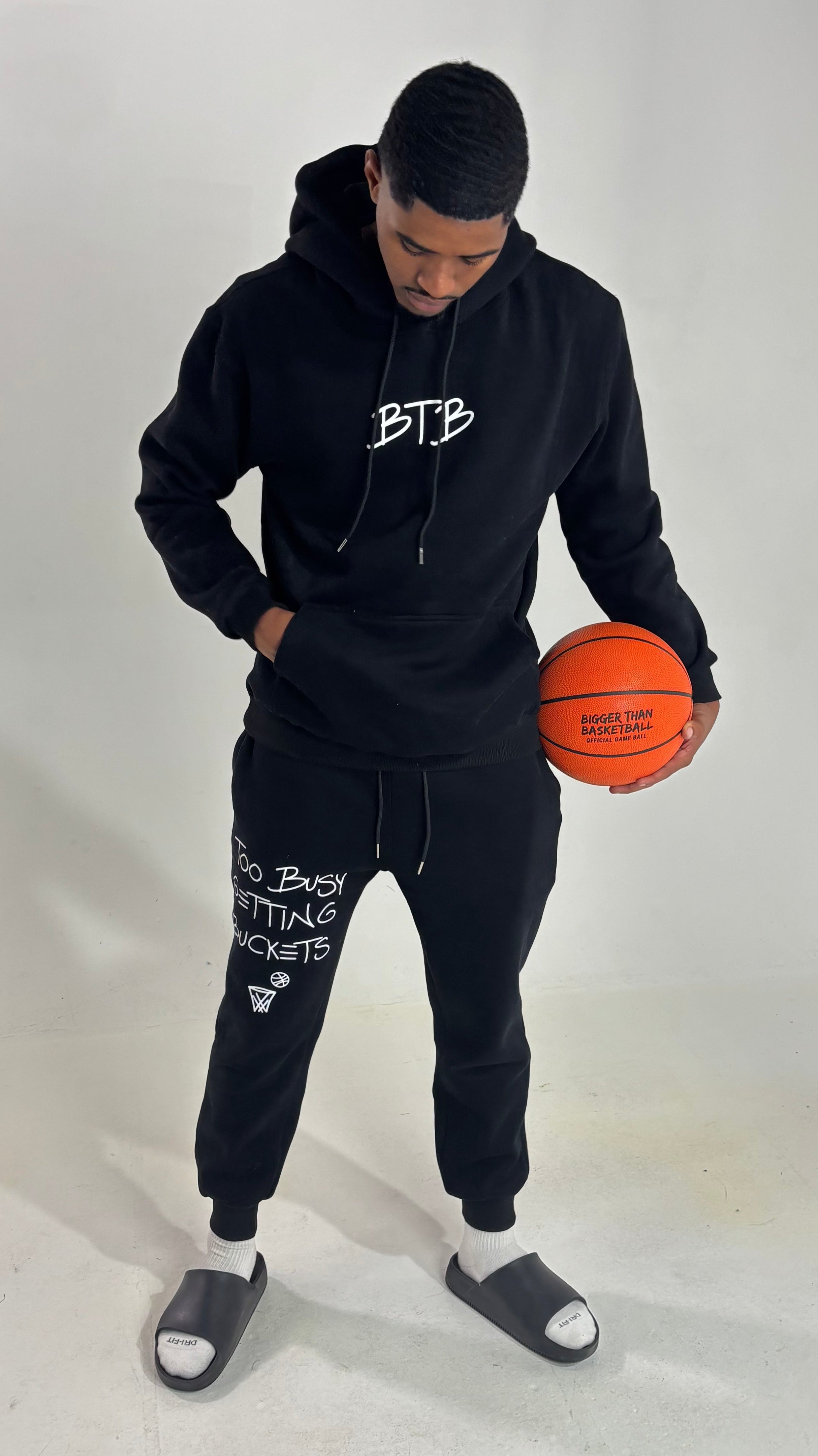 Collection of Person wearing a black hoodie and jogger set holding an orange basketball on a white background in a gallery layout