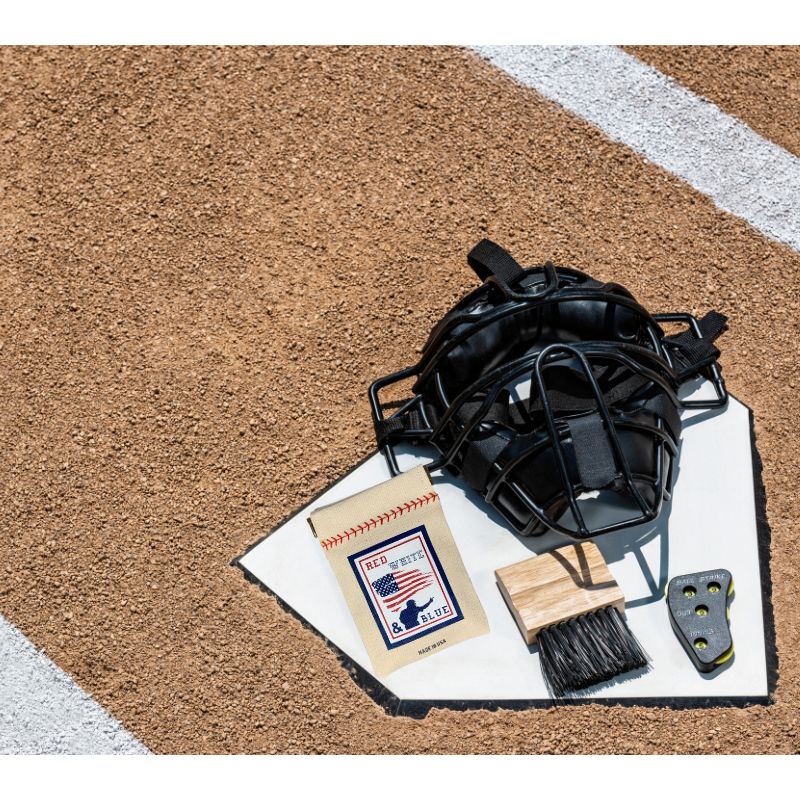 Baseball mask, cleaning brush, and cloth on a dirt surface with a white line.