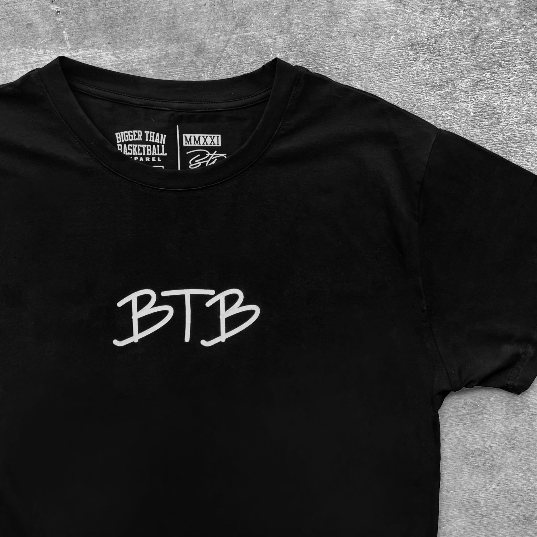 Black t-shirt with 'BTB' logo on a gray surface. Bigger Than Basketball.