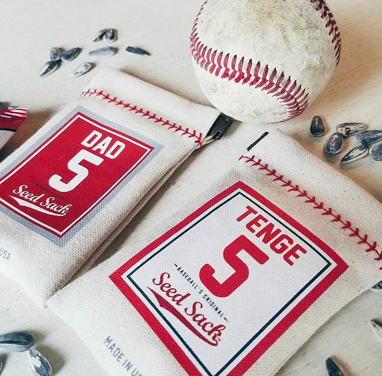 Two seed sacks with baseball design and text, accompanied by a baseball on a light background.