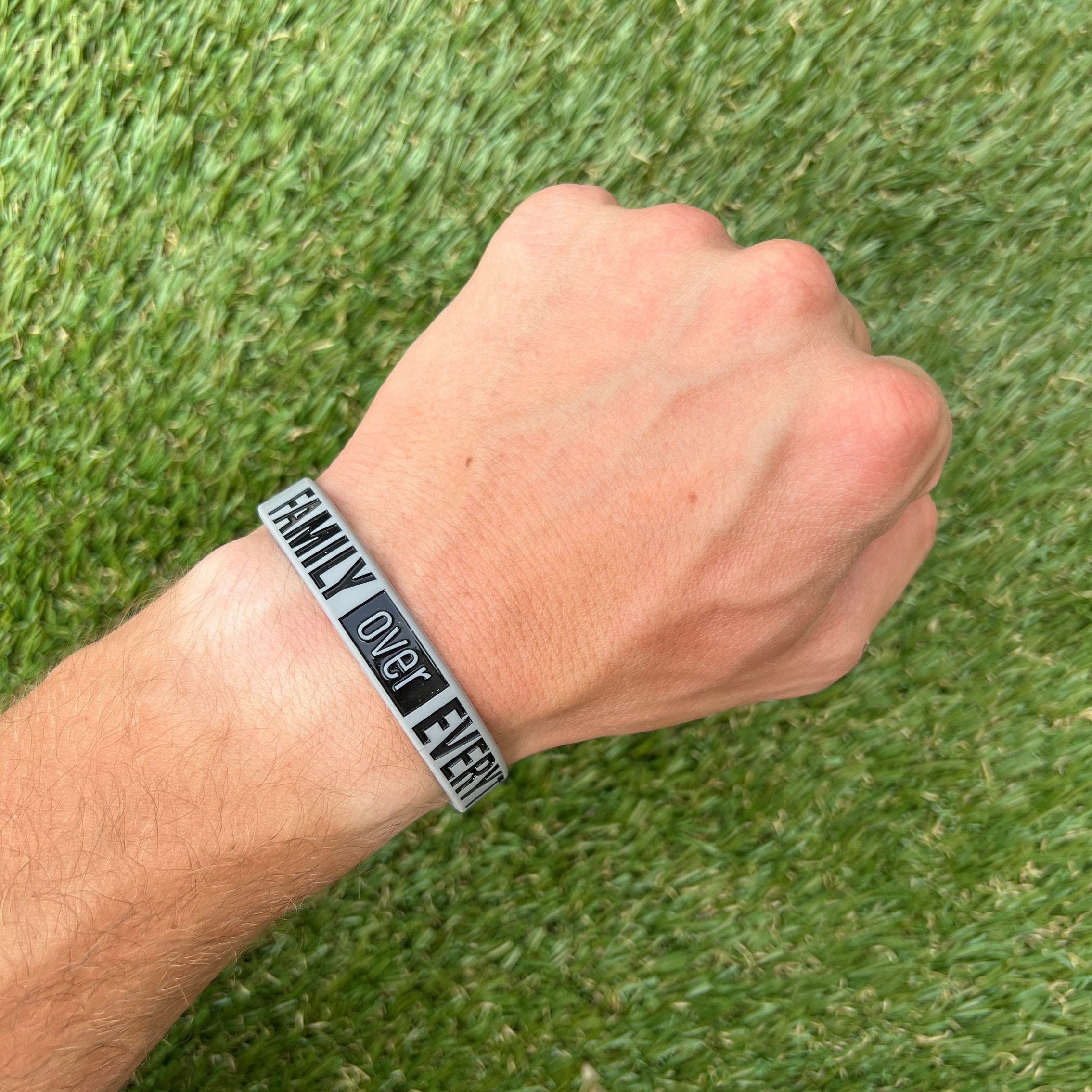 Collection of Hand wearing a bracelet with 'Family Over Everything' text on grass background in a gallery layout