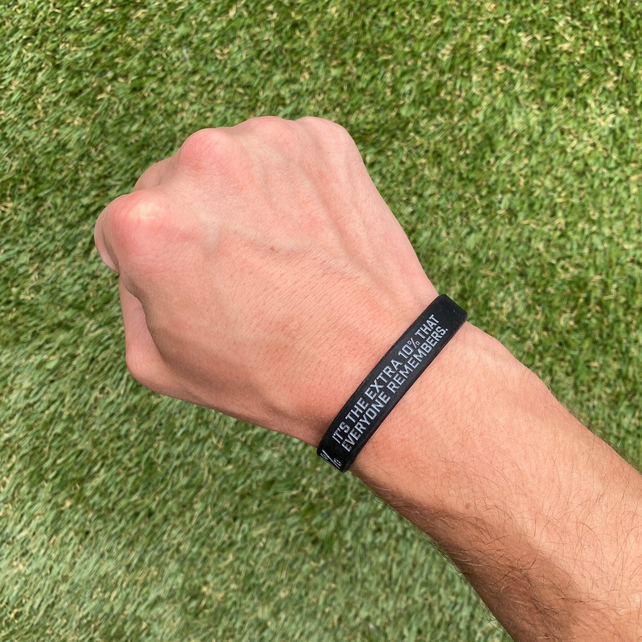 Collection of Hand wearing a black wristband with text on a grass background in a gallery layout