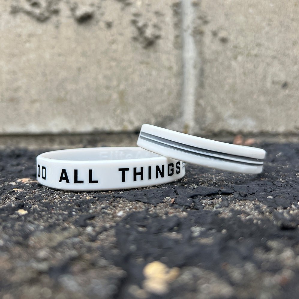 Two white wristbands with text on a concrete surface