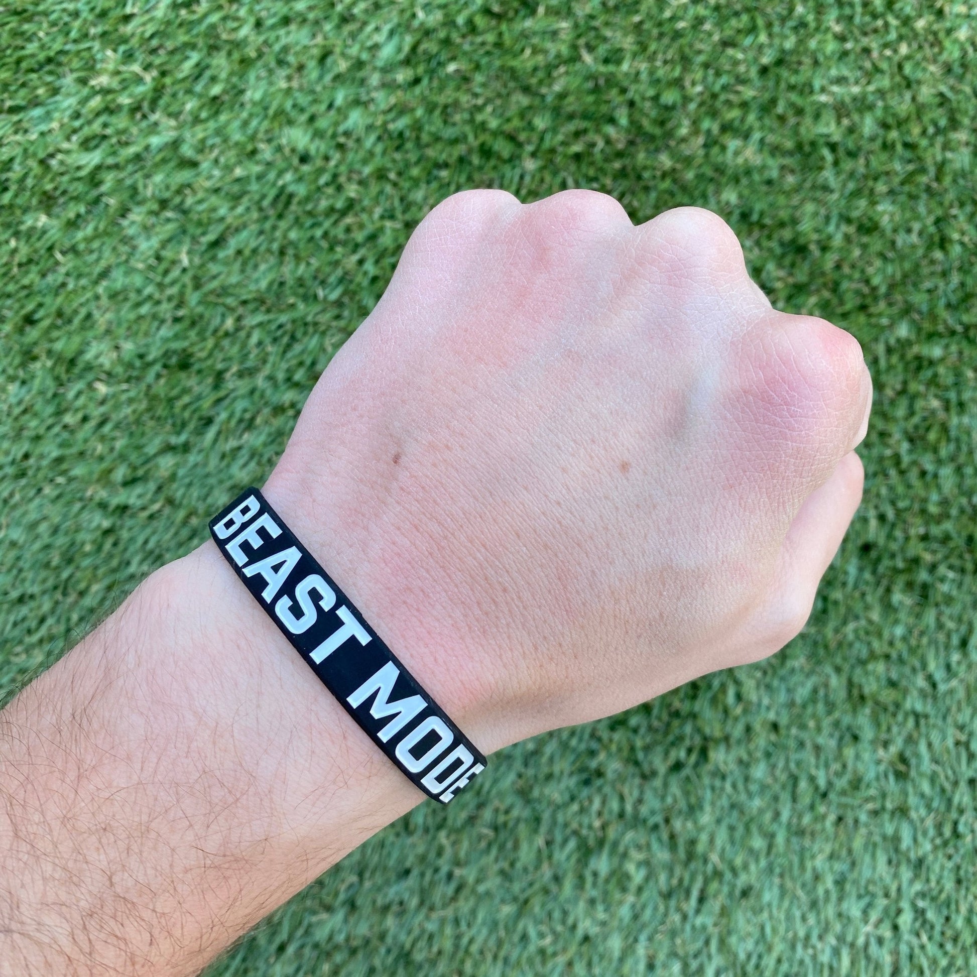 Hand wearing a 'BEAST MODE' wristband on a grass background